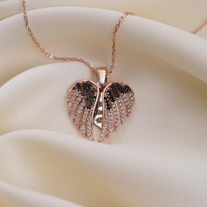A delicate necklace with a heart-shaped pendant featuring a pair of sparkling wings rests on a soft, white fabric.