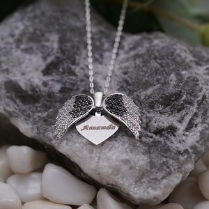 A silver necklace with a heart-shaped pendant featuring black gemstones is displayed on a rock, surrounded by small white pebbles.
