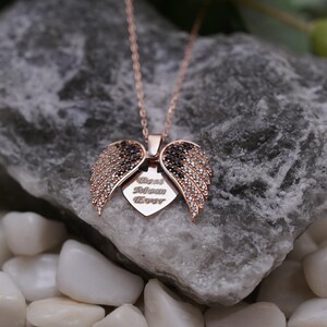 A necklace with a pendant featuring a pair of open wings, resting on a rock.
