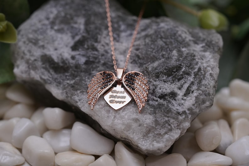 A necklace with a pendant featuring a pair of open wings, resting on a rock.