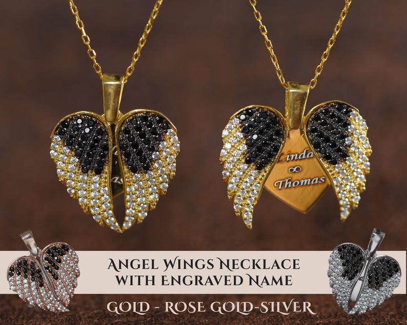 two angel wing necklaces with engraved names on them. The necklaces are made of gold, rose gold, and silver materials, and they are adorned with black and white gemstones. The necklaces are displayed against a brown background, and there is a text overlay that reads "ANGEL WING NECKLACE WITH ENGRAVED NAME GOLD - ROSE GOLD - SILVER".