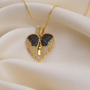 A gold-colored heart-shaped pendant with black and white diamonds is displayed on a white fabric surface.