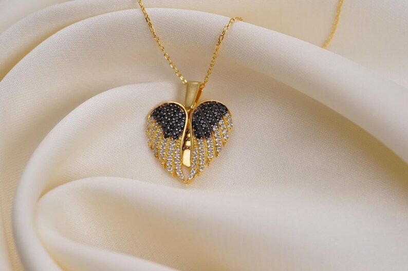 A gold-colored heart-shaped pendant with black and white diamonds is displayed on a white fabric surface.