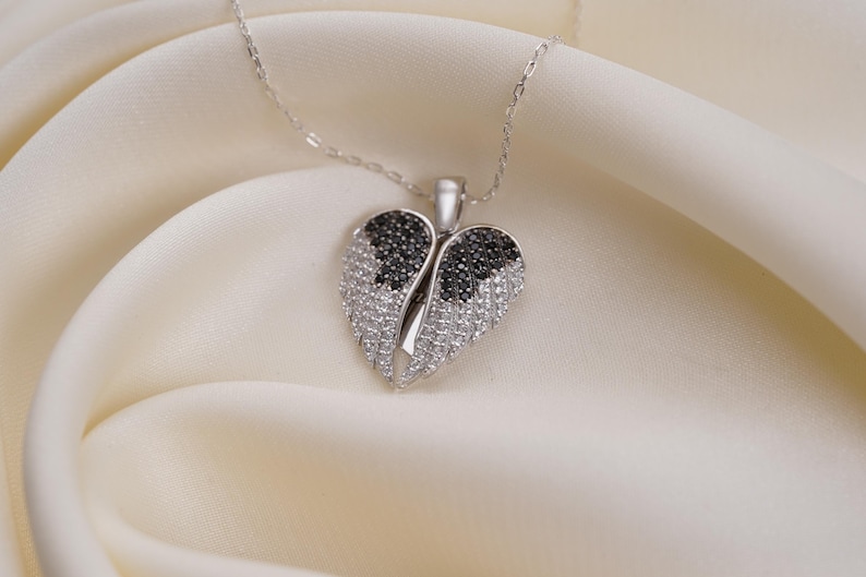 A silver necklace with a heart-shaped pendant adorned with black and white diamonds is displayed on a white fabric surface.