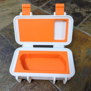 May include: A white plastic case with orange foam lining. The case has two latches on the top and a small handle on the side.