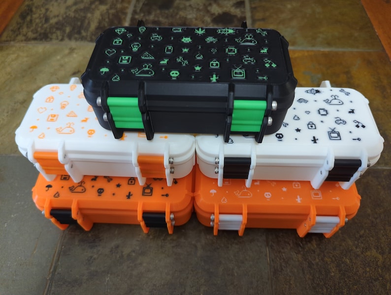 May include: Four stackable storage containers with different colored lids. The top container is black with green latches and has a white design of various icons. The second container is white with black latches and a white design of various icons. The bottom two containers are orange with black latches and a white design of various icons.