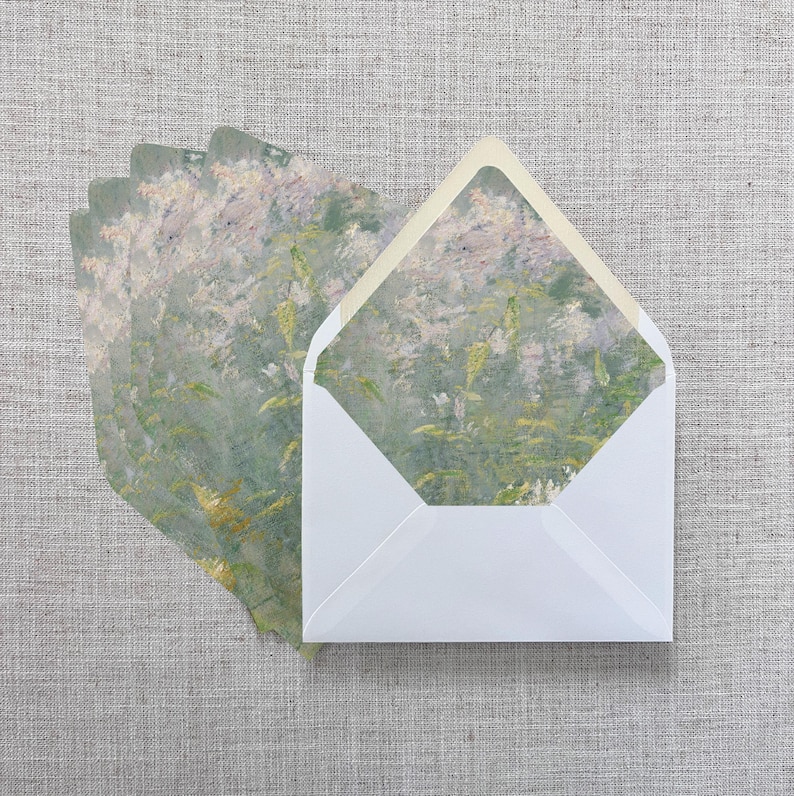 May include: White envelopes with a floral design on the inside, with a matching floral design on the cards. The cards and envelopes are arranged on a gray linen surface. The floral design features shades of green, yellow, and pink.