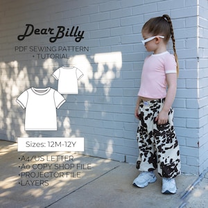 May include: A child wearing a pink t-shirt with white trim and cow-print pants stands next to a brick wall. The image includes a sewing pattern graphic with the text "Dear Billy" and details about the pattern, including sizes 12M-12Y.