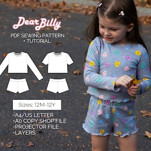 Op de afbeelding: Een jong meisje draagt een grijze pyjamaset met een hartjespatroon. De afbeelding toont ook een PDF-naaipatroon met de tekst "Dear Billy" en "PDF Sewing Pattern + Tutorial". Het patroon bevat ontwerpen voor een top met lange mouwen, een top met korte mouwen en shorts, in maten van 12 maanden tot 12 jaar.