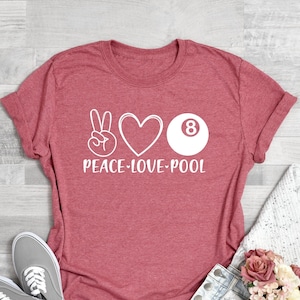 May include: Coral pink t-shirt with a white peace sign, heart, and 8-ball graphic. The text "Peace-Love-Pool" is printed below the graphic.