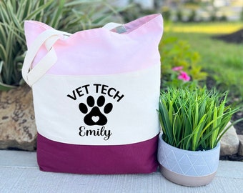 May include: A tri-colour tote bag with a pink, white and burgundy design. The bag has a black paw print with a heart in the centre and the text "Vet Tech Emily".