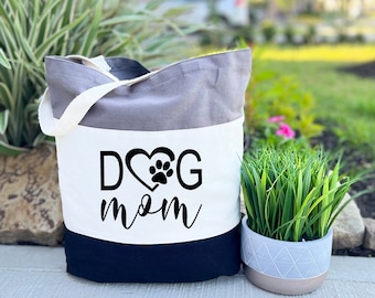 May include: A tri-color tote bag with a grey, white, and black design. The bag has a white panel with the text "DOG mom" in black lettering with a heart and paw print.