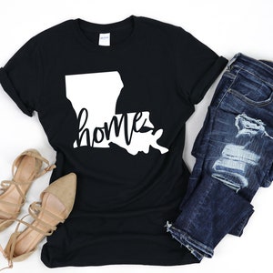 Pu&ograve; includere: Maglietta nera con un contorno bianco dello stato della Louisiana e la parola "home" scritta in bianco in corsivo.