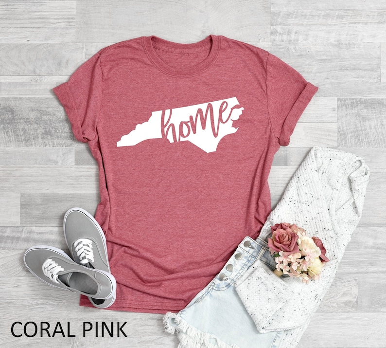 K&ouml;nnte beinhalten: Korallenrosa T-Shirt mit einem wei&szlig;en Umriss des Bundesstaates North Carolina und dem Wort "home" innerhalb des Bundesstaates.