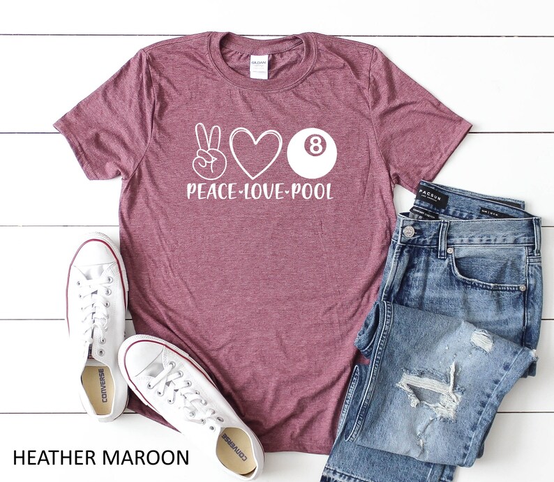 May include: Heather maroon t-shirt featuring a white peace sign, heart, and 8-ball graphic. The text "Peace-Love-Pool" is printed below the graphic. The shirt is styled with blue jeans and white trainers.