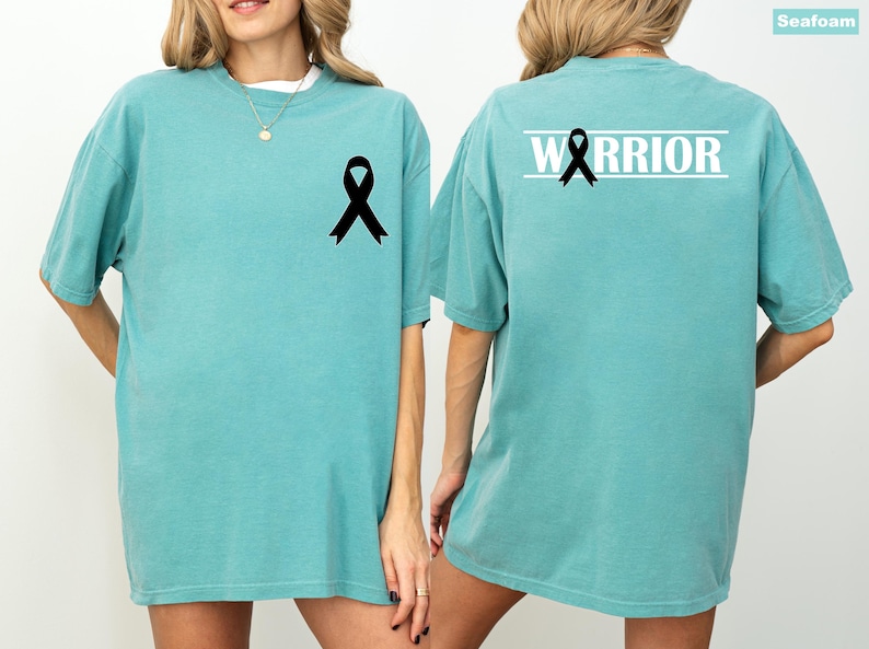 May include: Seafoam green t-shirt with a black ribbon graphic on the front and back. The back of the shirt features the word "WARRIOR" in white block letters above the ribbon. The shirt is a comfortable, oversized fit.