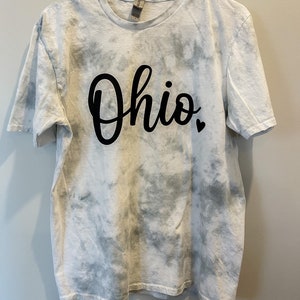 May include: White tie-dye t-shirt with black lettering that says "Ohio" with a small black heart.