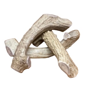 May include: Three natural antler dog chews, each with a different shape and size. The antlers are light brown and have a rough texture.