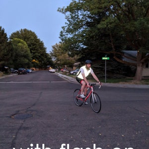May include: A person riding a red road bicycle on a paved street at dusk. The cyclist wears a reflective vest and helmet for safety. The image includes the text "with flash on".