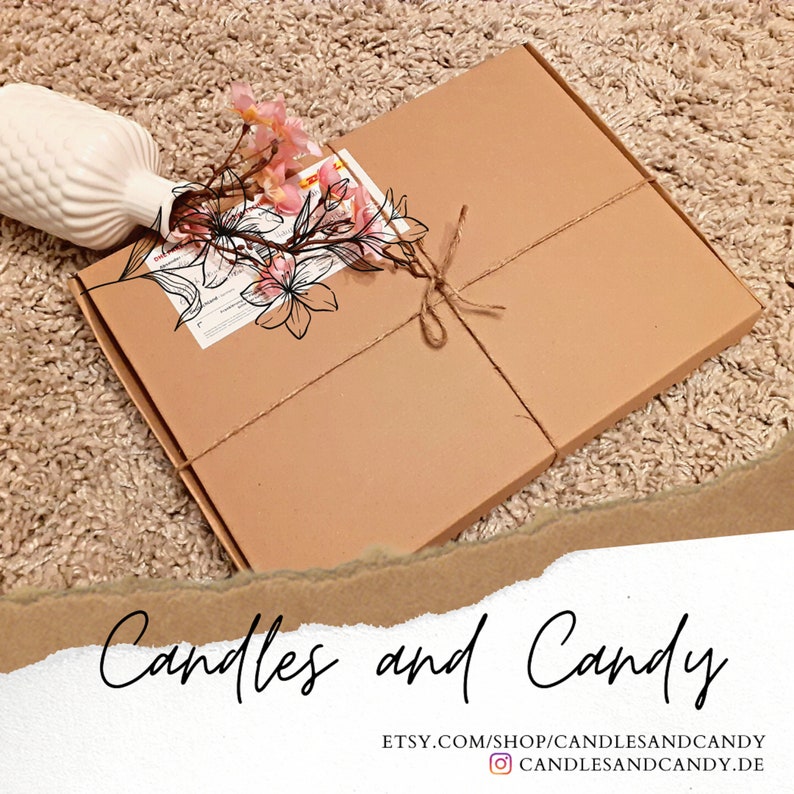 Puede incluir: Una caja de cart&oacute;n marr&oacute;n atada con cuerda y decorada con una ilustraci&oacute;n de una flor rosa. La caja est&aacute; etiquetada con "Candles and Candy" y el texto "Etsy.com/shop/candlesandcandy" y "@candlesandcandy.de".