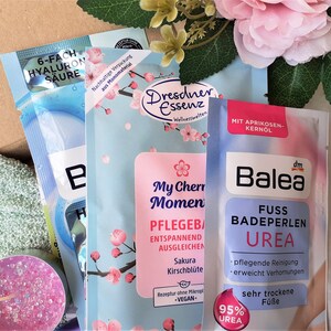 Puede incluir: Tres productos de ba&ntilde;o diferentes en paquetes individuales. El primer paquete es azul y blanco con el texto "6-fach Hyaluron S&auml;ure". El segundo paquete es azul y rosa con un dise&ntilde;o floral y el texto "My Cherry Moment Pflegebad Entspannend Ausgleichen Sakura Kirschbl&uuml;te Rezeptur ohne Mikroplastik -VEGAN-". El tercer paquete es azul y blanco con el texto "Balea Fuss Badeperlen Urea 95% Urea pfelgende Reinigung erweicht Verhornungen sehr trockene F&uuml;sse".