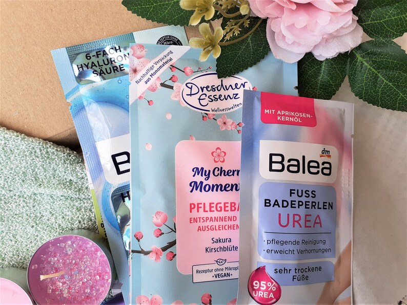 Puede incluir: Tres productos de ba&ntilde;o diferentes en paquetes individuales. El primer paquete es azul y blanco con el texto "6-fach Hyaluron S&auml;ure". El segundo paquete es azul y rosa con un dise&ntilde;o floral y el texto "My Cherry Moment Pflegebad Entspannend Ausgleichen Sakura Kirschbl&uuml;te Rezeptur ohne Mikroplastik -VEGAN-". El tercer paquete es azul y blanco con el texto "Balea Fuss Badeperlen Urea 95% Urea pfelgende Reinigung erweicht Verhornungen sehr trockene F&uuml;sse".