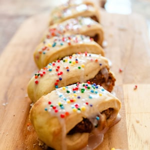 May include: A close-up of a wooden board with six cookies topped with white icing and colorful sprinkles. The cookies are arranged in a row, with the closest cookie in focus.