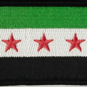 May include: A green, white and black embroidered patch with three red stars. The patch is a representation of the Syrian flag.