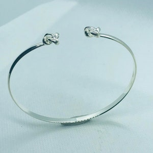 May include: A silver bangle bracelet with two knot-shaped accents on either end.