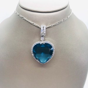 May include: A silver chain necklace with a large blue heart pendant encrusted with clear cubic zirconia stones.