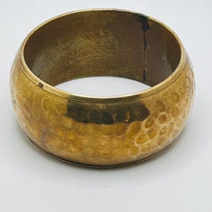May include: A hammered brass bangle bracelet with a smooth, polished finish. The bracelet is a simple, classic design that can be worn with any outfit.
