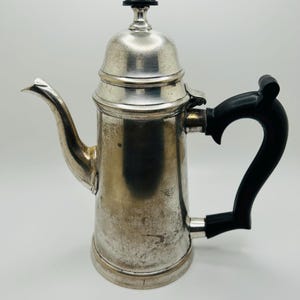 May include: Silver coffee pot with a black handle and a domed lid. The pot has a shiny, aged finish.