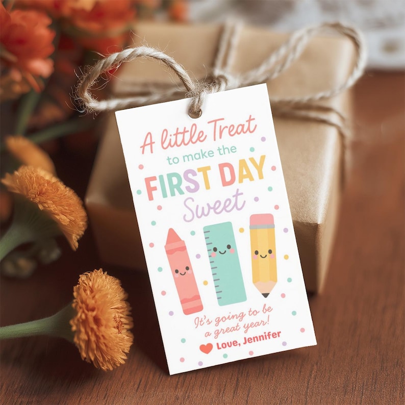 May include: A gift tag with the text "A little Treat to make the FIRST DAY Sweet." The tag features illustrations of a crayon, ruler, and pencil. The tag is tied to a wrapped gift with twine.