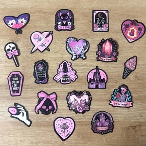 May include: A collection of stickers with a gothic theme, featuring a butterfly, cat, hearts, a skull, a coffin, a lipstick, a castle, and an ice cream cone. Some stickers have text like "Cute & Spooky" and "Your Coffin or Mine?"