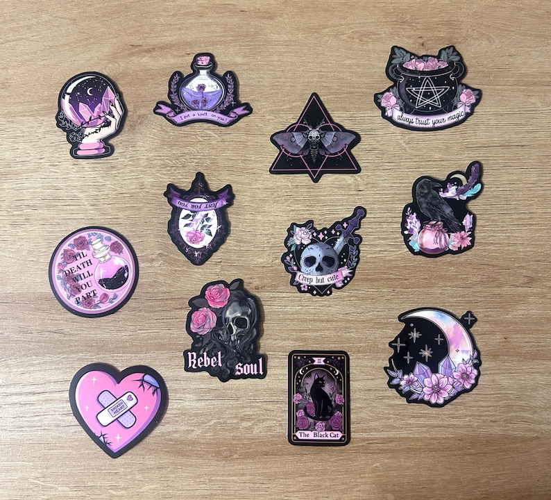May include: A collection of gothic-themed stickers featuring various designs. Includes a crystal ball, potion bottles, a moth, a cauldron with a pentagram, a raven, a skull with roses, a heart with a bandage, and a tarot card with a black cat. The stickers have a dark color palette.