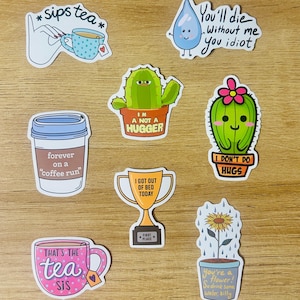 May include: A collection of colorful stickers with various designs and text. The stickers include a hand holding a teacup, a coffee cup, a cactus, a water droplet, a trophy, a teacup, and a sunflower in a pot. The text includes phrases like "sips tea" and "I got out of bed today."