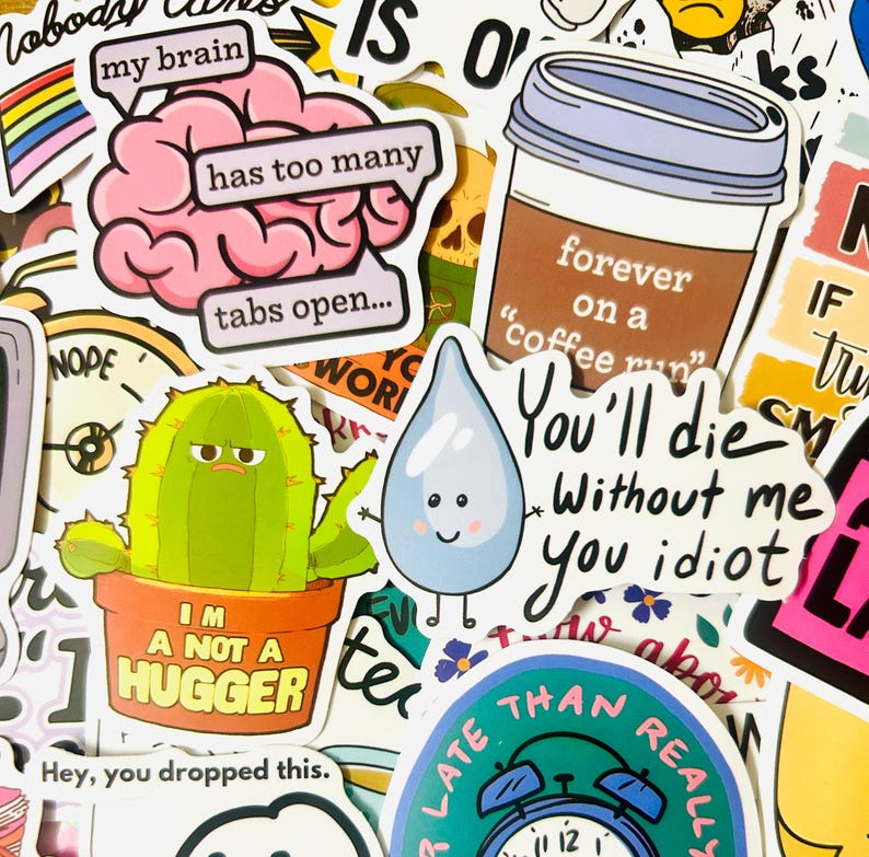 May include: A collection of colorful stickers with various designs and text. Includes a pink brain with the text "my brain has too many tabs open...", a cactus in a pot that says "I'm not a hugger", and a coffee cup that says "forever on a coffee run".