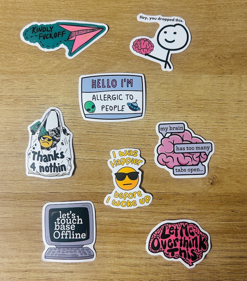 May include: A collection of colorful stickers with humorous phrases and graphics. Designs include a paper airplane, a brain, an alien, a shopping bag, a computer, and an emoji wearing sunglasses. Text includes "Kindly F*ck Off", "Hello I'm Allergic to People", and "Let Me Overthink This."