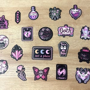May include: A collection of gothic-themed stickers with various designs, including a castle, potion bottles, crystals, a coffin with ghosts, and a butterfly with a skull. The stickers feature pink, purple, and black colors, with text like "Goth queen" and "not a phase".