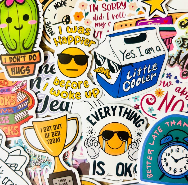 May include: A collection of colorful stickers with various designs and text. Stickers include a cactus, a cooler, a trophy, and an alarm clock. Text includes "I don't do hugs", "I was happier before I woke up", and "Everything is ok".