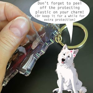 May include: A clear acrylic charm with a character design, attached to a gold-colored keyring. The charm is shown with its protective plastic being peeled off. A cartoon white dog with a flower crown is also in the image.