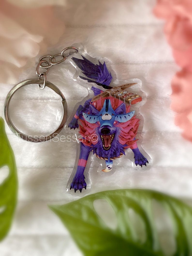 May include: A colorful wolf keychain with a silver keyring. The wolf has a fierce expression with open mouth and sharp teeth. The wolf's fur is a mix of purple, pink, and blue. The keychain is a unique accessory.