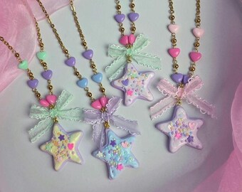 May include: Four necklaces featuring gold-tone chains adorned with small pastel heart beads. Each necklace includes a star-shaped pendant decorated with colorful sprinkles and small star accents, finished with a delicate fabric bow at the top.