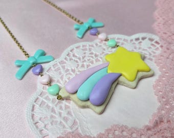 May include: A gold-tone chain necklace featuring a central shooting star pendant with a yellow star and pastel purple, blue, and pink trails. The chain is accented with small light blue bows and tiny heart-shaped beads in purple, pink, and green.