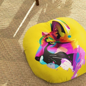 May include: A yellow round floor pillow with a colorful abstract illustration of a cat's face. The cat's fur is pink, orange, blue, and green.