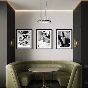 May include: Three black framed photographs of a woman in a black and white setting. The woman in the left photo is holding a glass of wine and wearing a ring. The woman in the center photo is wearing sunglasses and a white towel. The woman in the right photo is wearing a black dress and a pearl necklace.