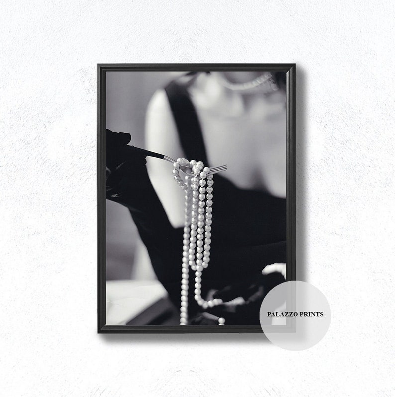 May include: A black and white photograph of a woman wearing a black dress and holding a string of pearls on a fork.