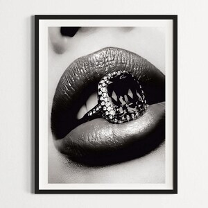 May include: Black and white framed print featuring a close-up of glossy lips with a large diamond ring. The ring has a large, dark-colored center stone surrounded by smaller, clear stones. The image is a high-contrast, artistic photograph.
