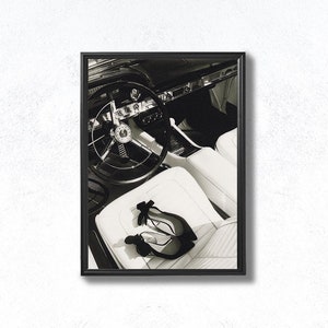 May include: Black and white photo of the interior of a classic car with a steering wheel and two pairs of black high heels on the white leather seat.