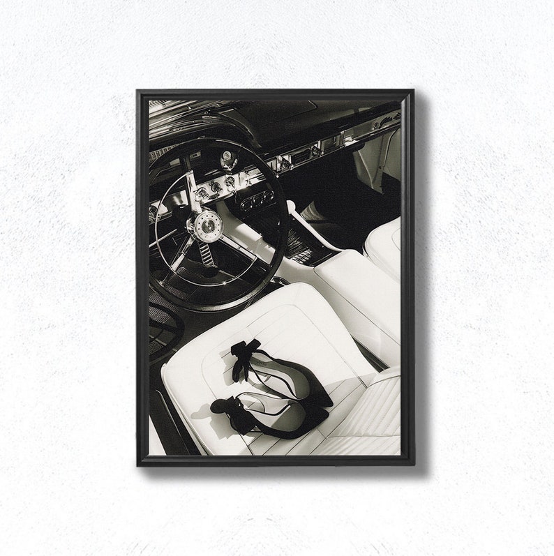 May include: Black and white photo of the interior of a classic car with a steering wheel and two pairs of black high heels on the white leather seat.